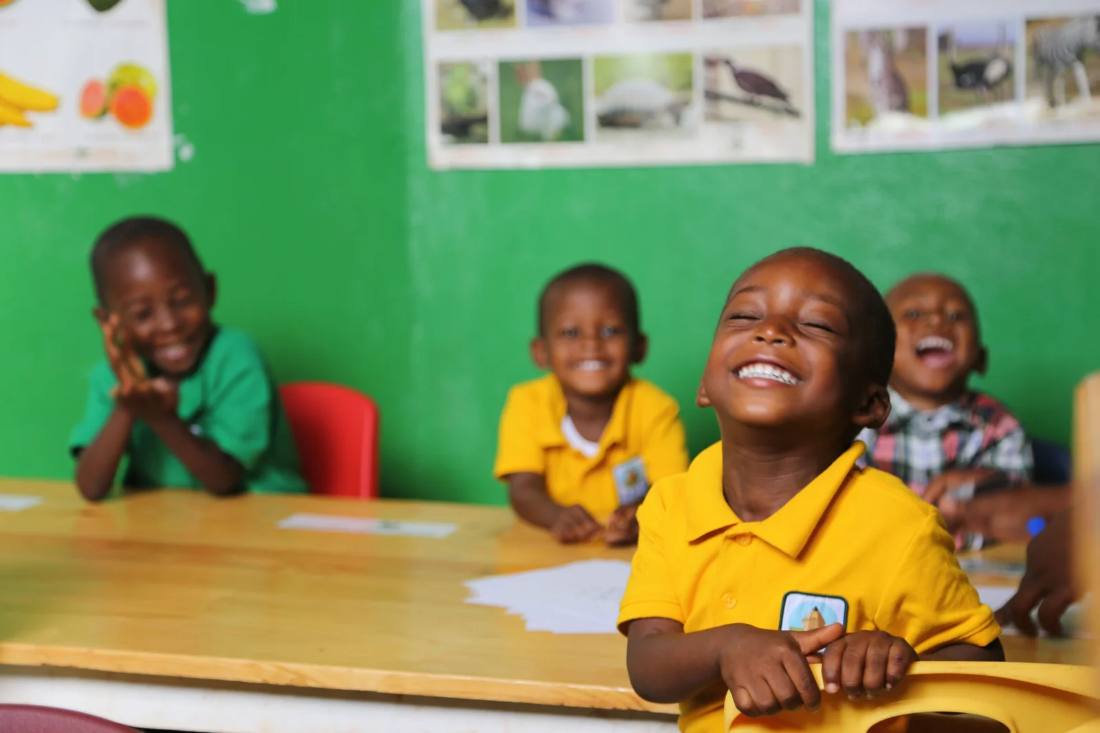 A child in a yellow uniform laughing with classmates at BATI School